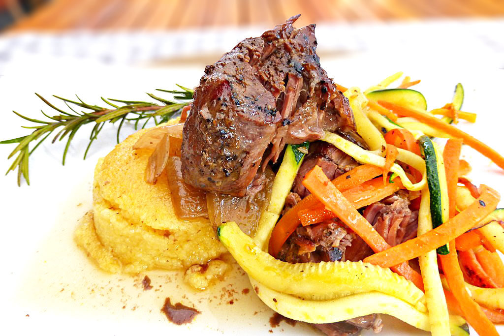 side view of a plate with polenta, vegetables and brisket