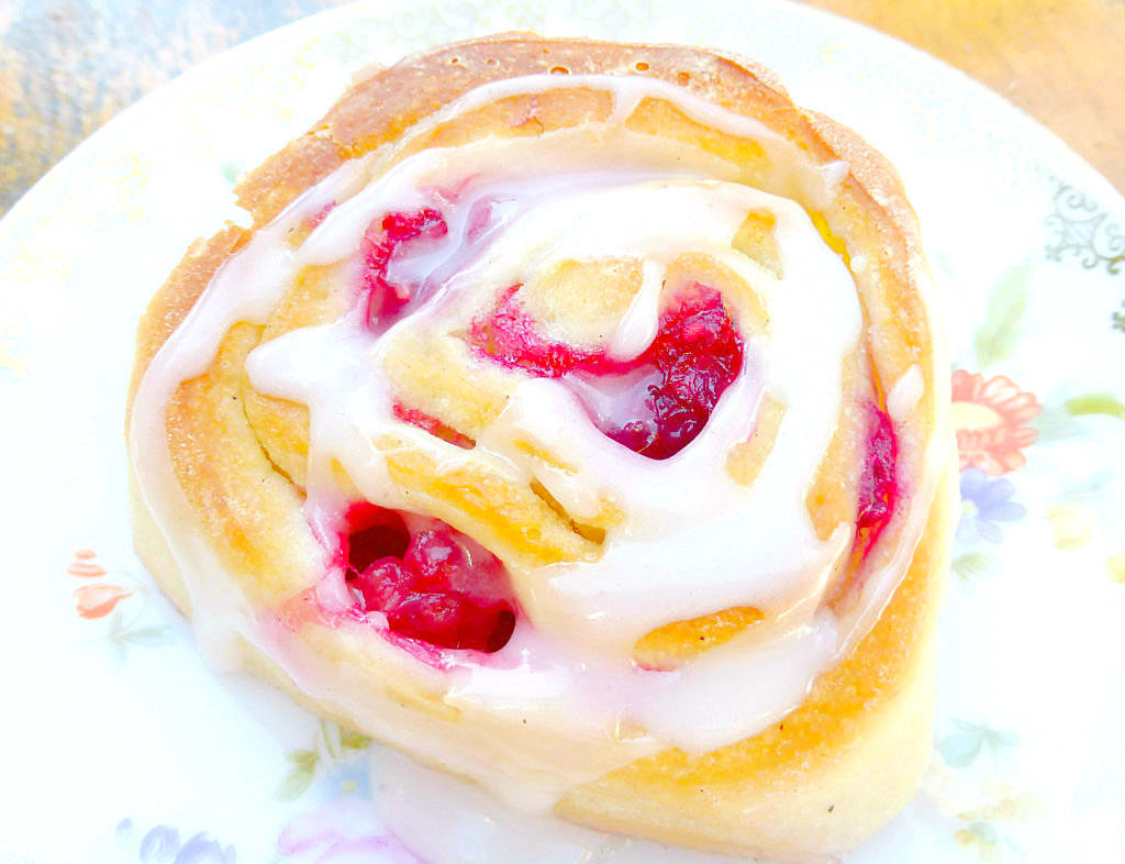 close up of a sweet bread bun with raspberries and a vanilla drizzle