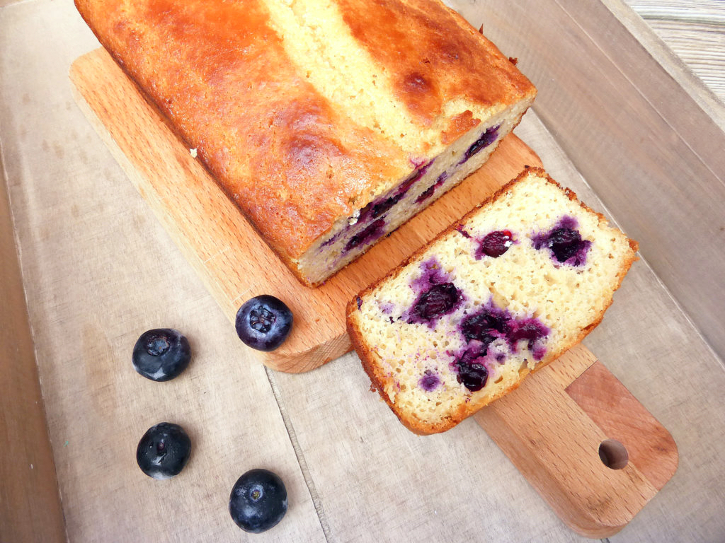 lemon and blueberry loaf cake with a slice on a wooden board