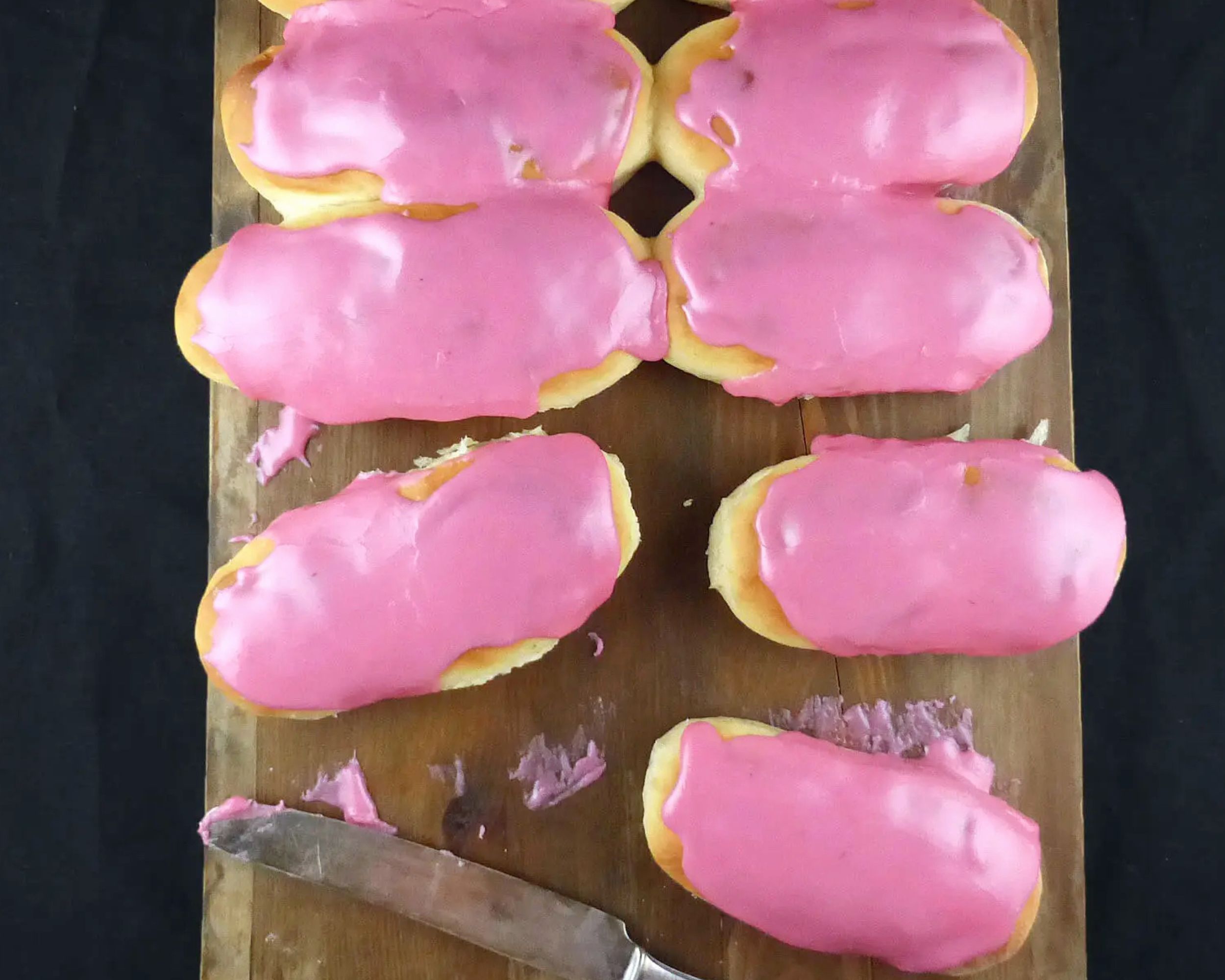 pink iced finger buns on a wooden board