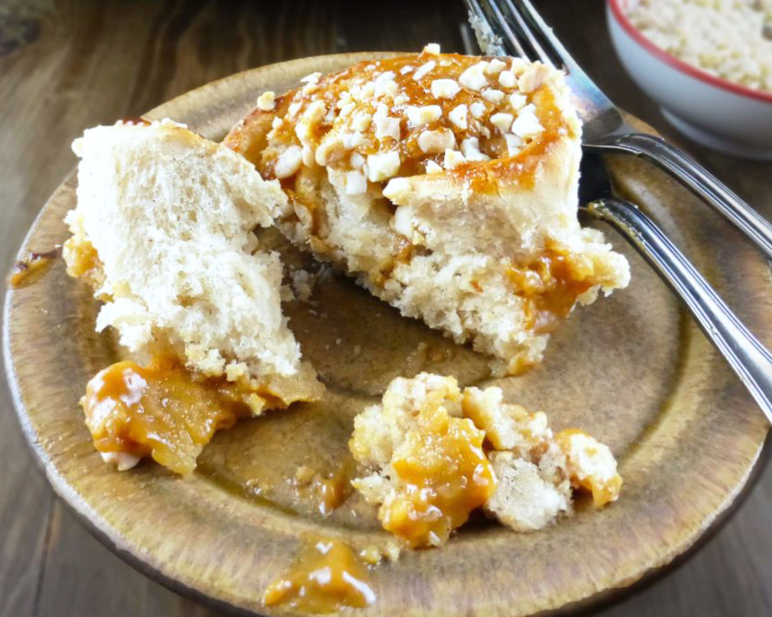 close up of a sticky bun on a golden coloured plate, on top of a wooden board.