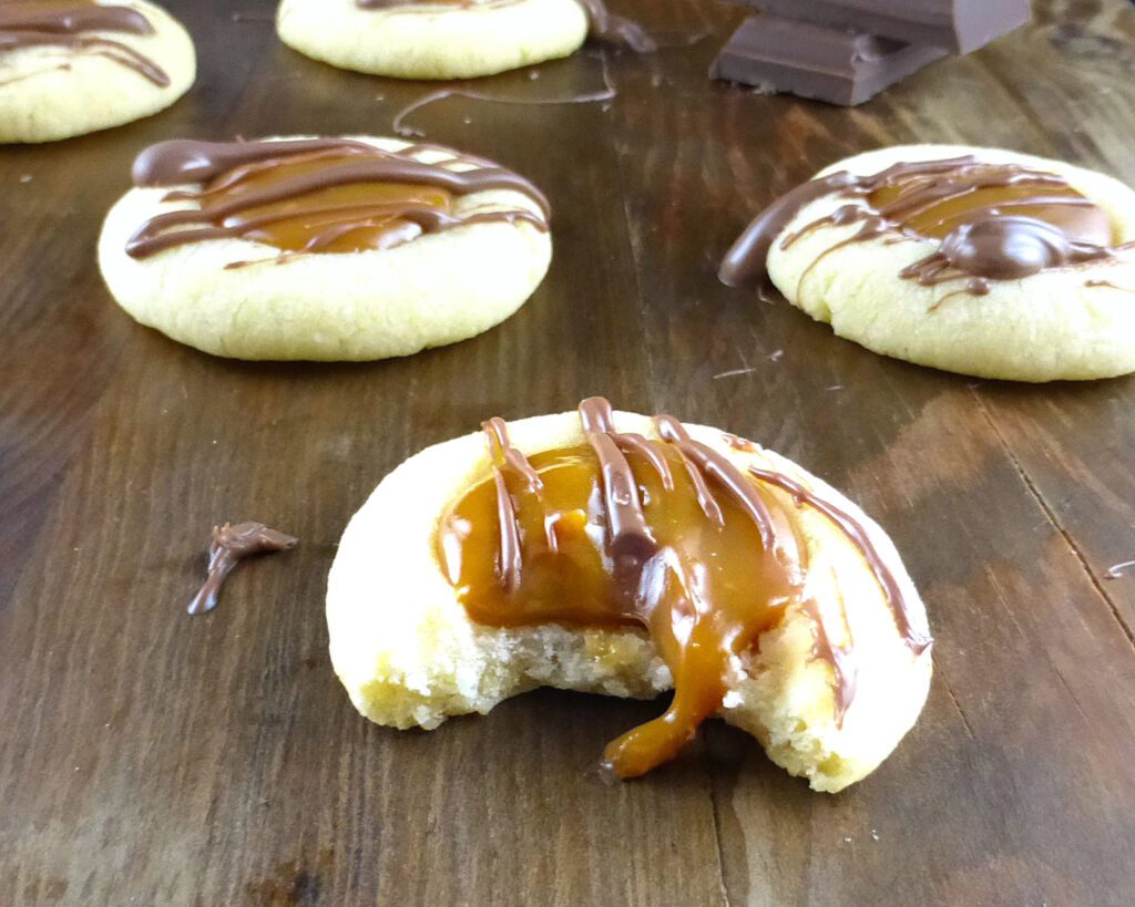 caramel thumbprint cookie with a bite taken out on a wooden board