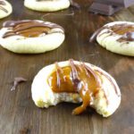 caramel thumbprint cookie with a bite taken out and drizzled with chocolate on a wooden board