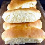 homemade hotdog buns stacked up on a wooden board