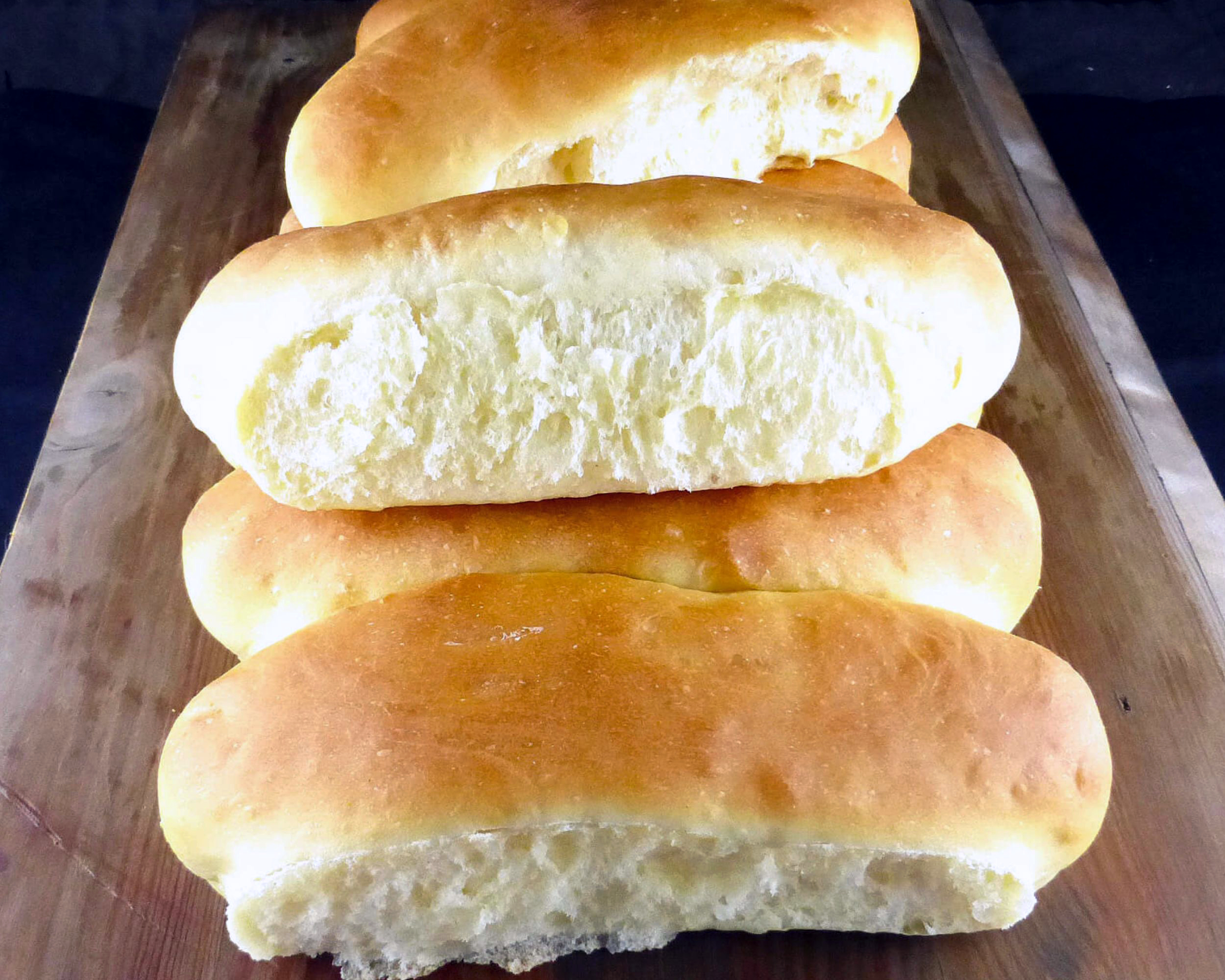 homemade hotdog buns stacked up on a wooden board 