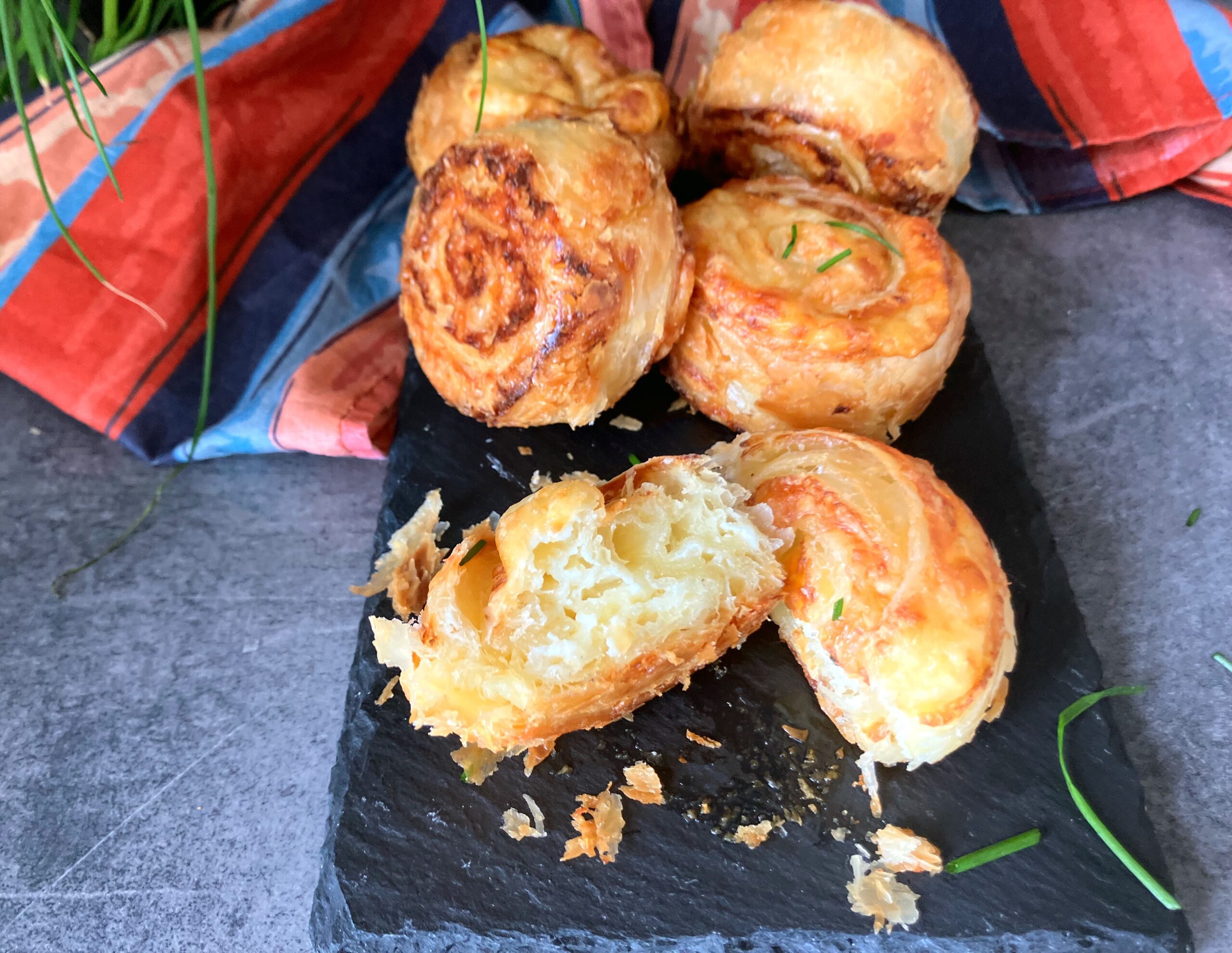cheese puff pastries on a slate board with one cut open and a multicolored cloth