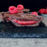 dark chocolate tartlet on slate with raspberry on top and a black background