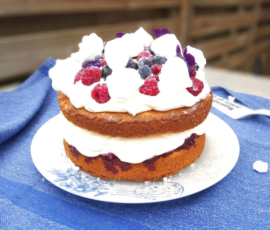 a layer cake covered in cream and berries on a blue cloth