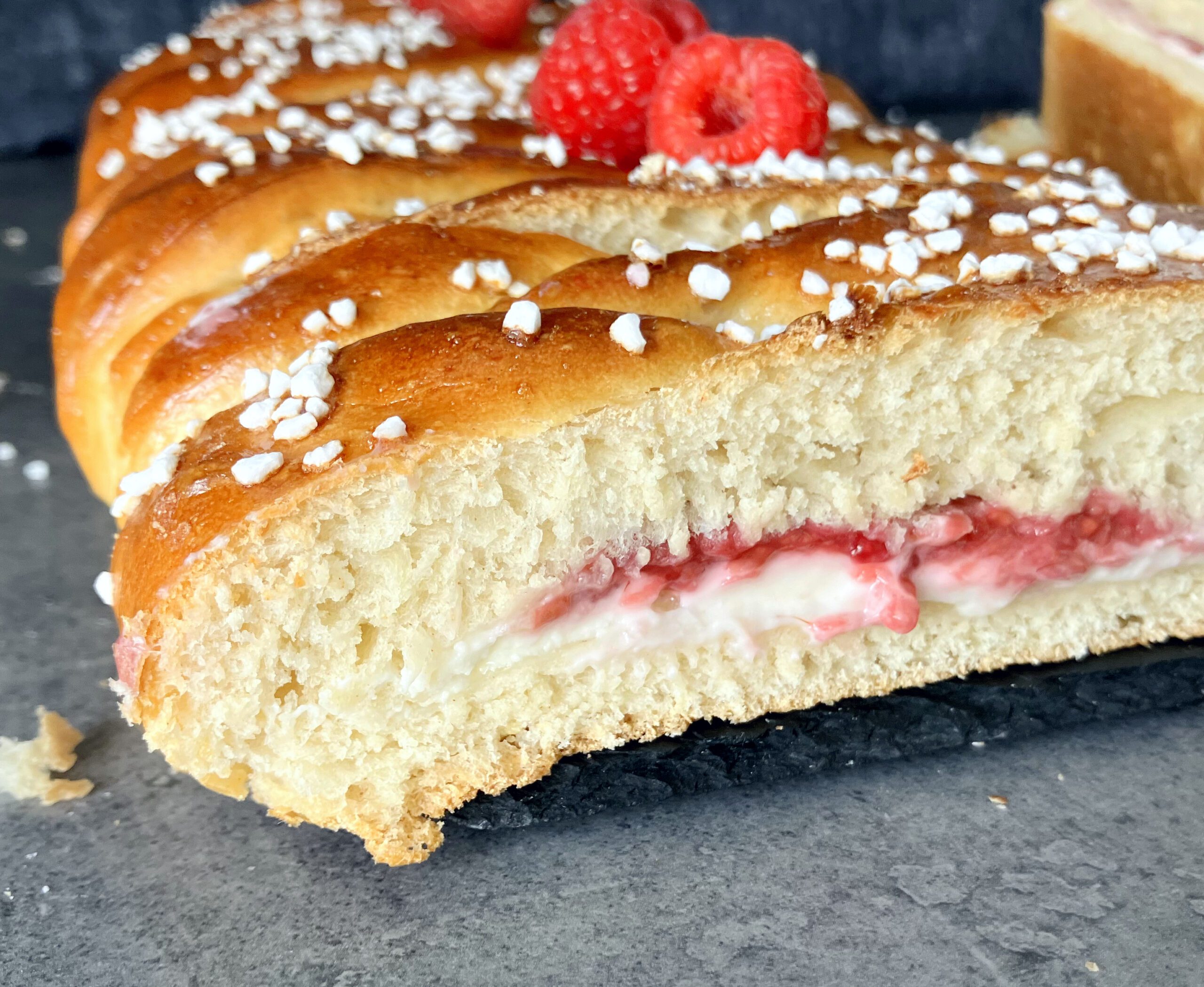 close up side view of a bread braid with raspberries and cream cheese with a dark blue background